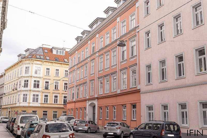 Blick auf die historische Straße mit dem orangeroten Eckgebäude und parkenden Autos.