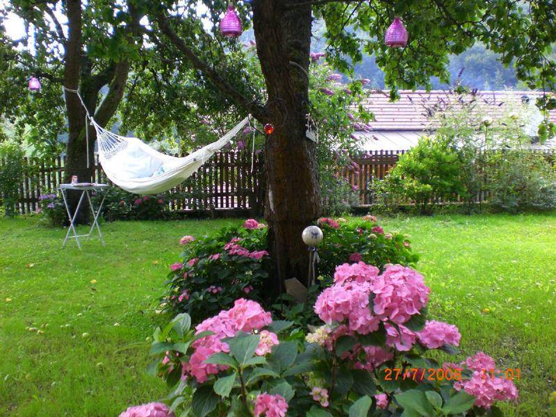 Entspannender Gartenbereich mit Hängematte unter Bäumen und üppigen rosa Hortensien.