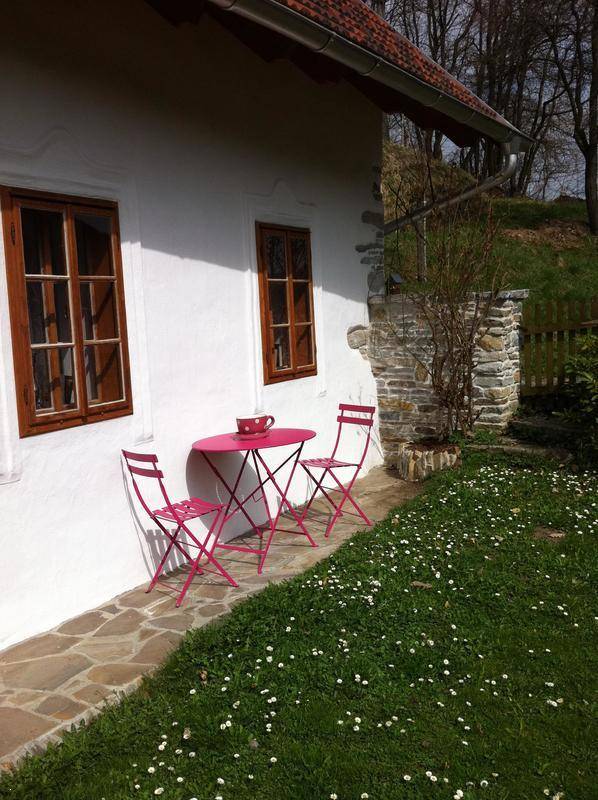 Rosa Gartentisch und Stühle auf der Steinterrasse neben dem Haus mit Blick ins Grüne.