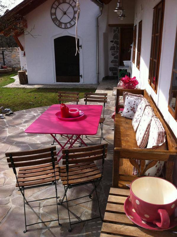 Sonnige Steinterrasse mit Holzsitzbank, rosa Tisch und Stühlen, perfekt für entspannte Stunden.