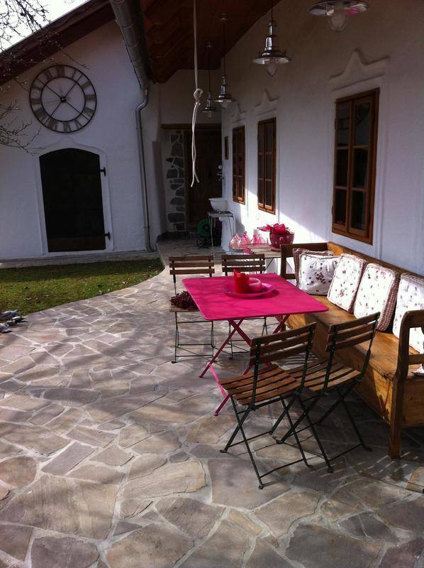 Gemütliche Steinterrasse mit Holzsitzbank, rosa Tisch und Stühlen, ideal für Mahlzeiten im Freien.