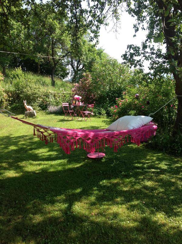 Entspannungsbereich im Garten mit Hängematte und kleiner Sitzgruppe unter Bäumen.