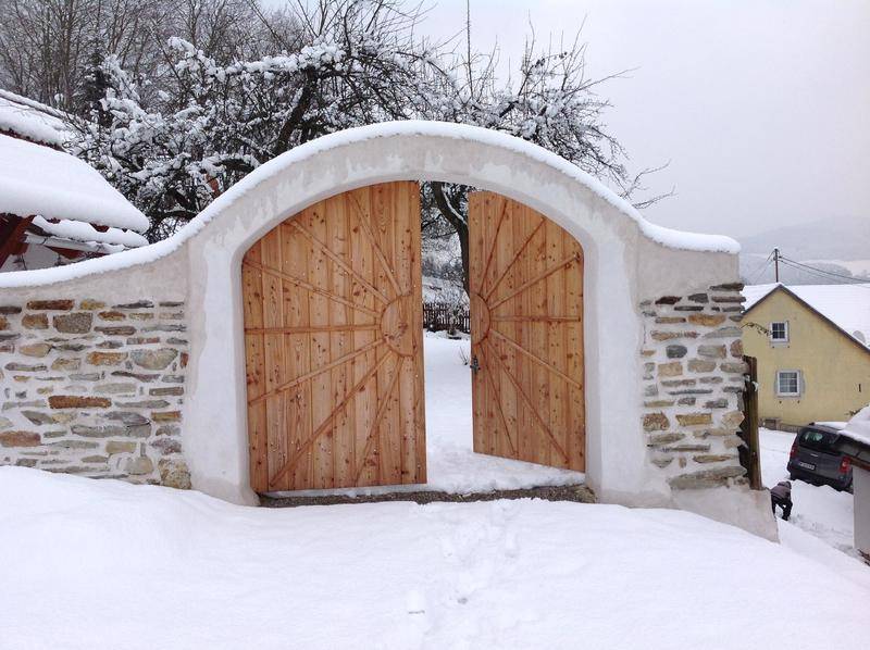 Rustikales Holztor in einer Steinmauer, umgeben von Schnee und Winterlandschaft.