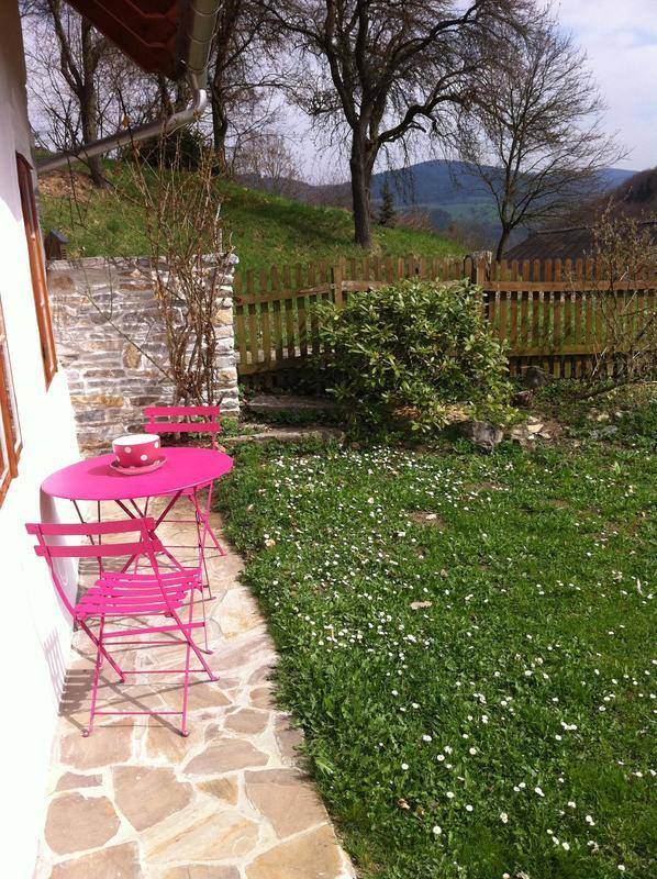 Kleiner rosa Gartentisch auf der Steinterrasse mit Blick auf die grüne Hügellandschaft.