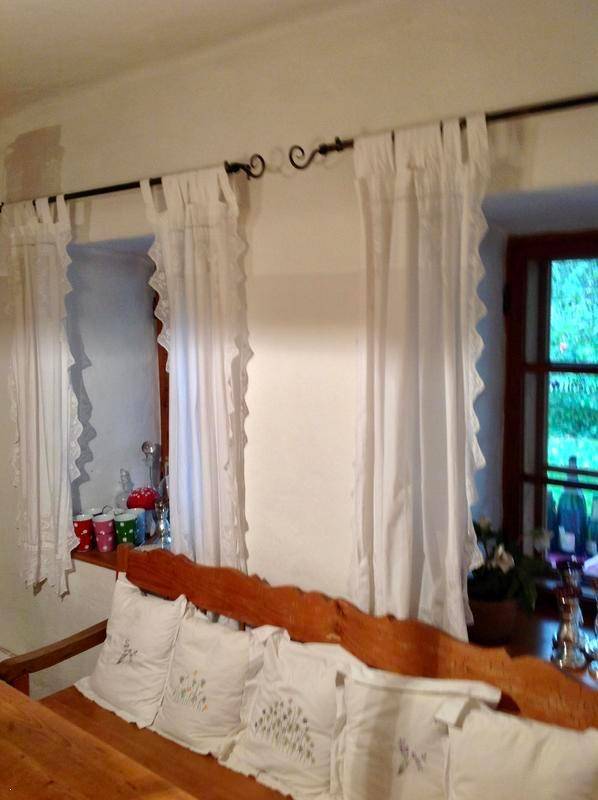Helle Fenster mit weißen Rüschenvorhängen und einer traditionellen Holzbank im Wohnzimmer.