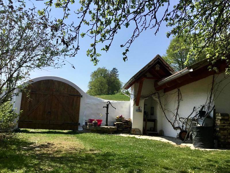 Ländliches Anwesen mit weiß getünchter Fassade, Holztor und einem alten Wasserbrunnen im Garten.