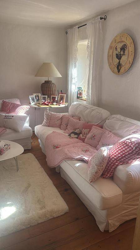 Gemütliches Wohnzimmer mit weißen Sofas, rosa karierten Decken und einem flauschigen Teppich.