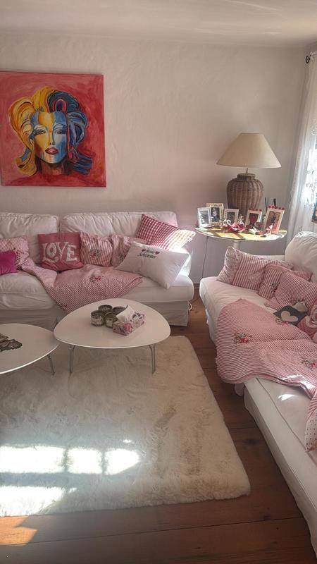 Helles Wohnzimmer mit weißen Sofas, rosa Akzenten und einem modernen Kunstwerk an der Wand.