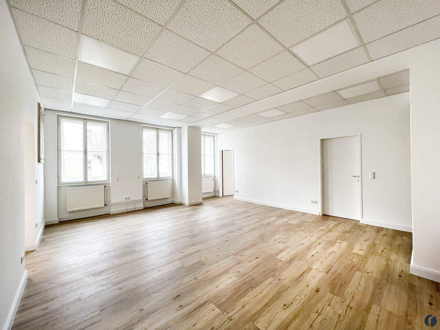 Großer, heller Büroraum mit mehreren Fenstern, Laminatboden und weißen Wänden, bezugsfertig.