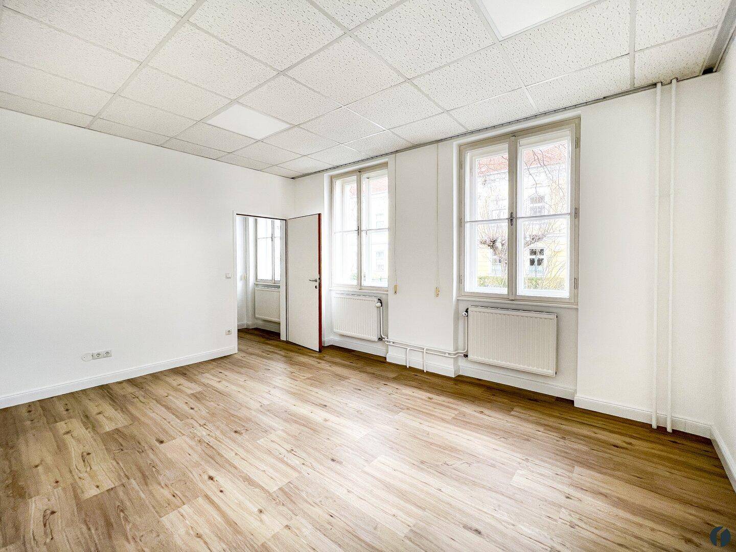 Helles Büro mit zwei großen Fenstern, Laminatboden und weißen Wänden, ideal für Einzelbüros.