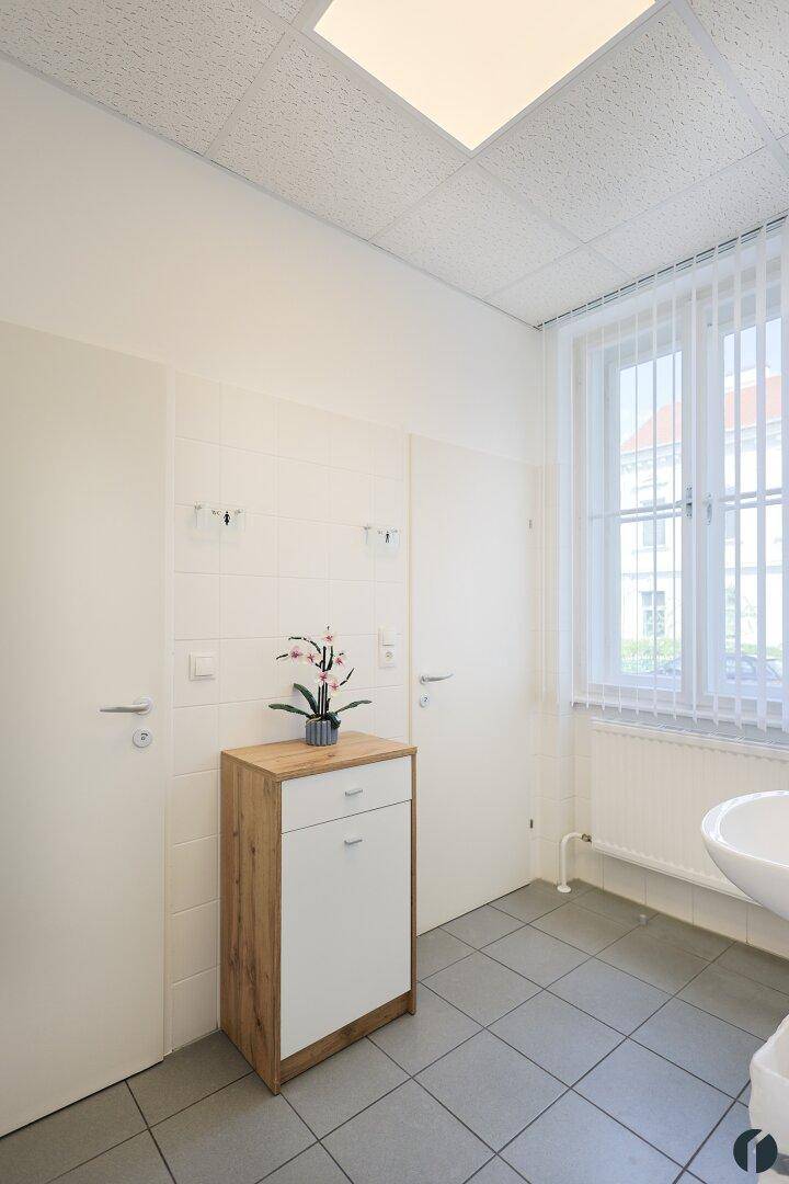 Helles Badezimmer mit Fenster, Waschbecken und grauen Fliesen, ausgestattet mit einem Holzschrank.