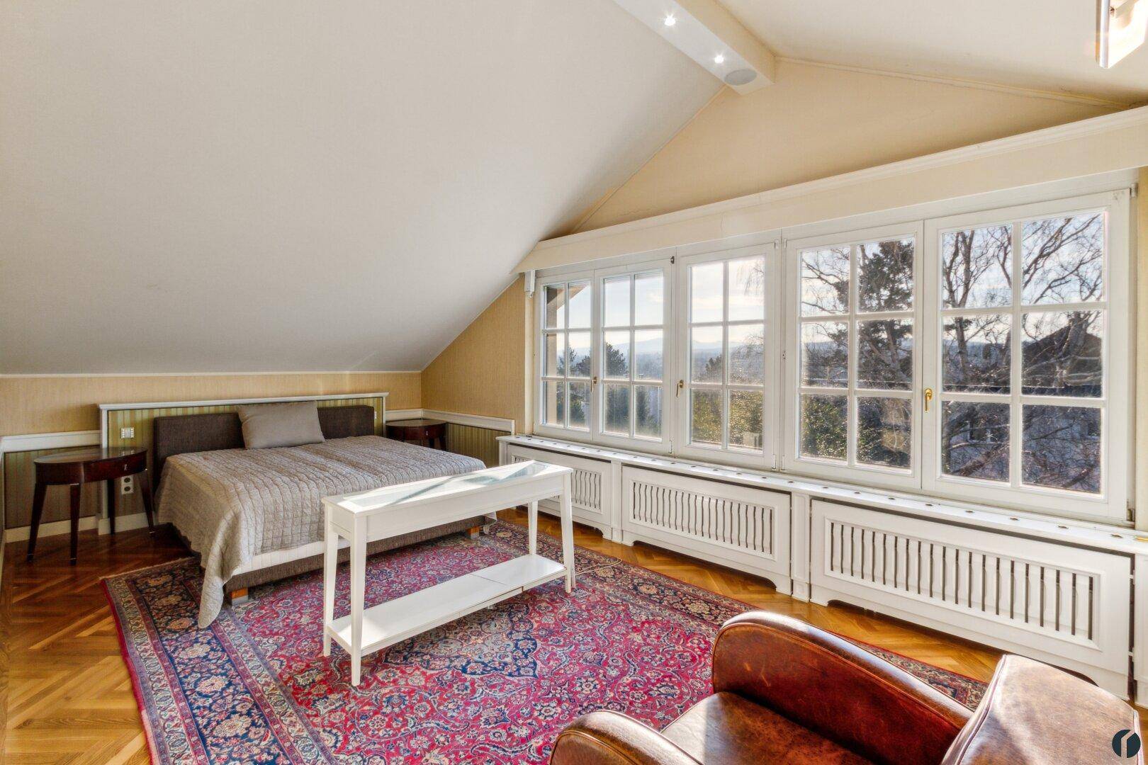Helles Schlafzimmer im Dachgeschoss mit großen Fenstern, Parkettboden und Bergblick.