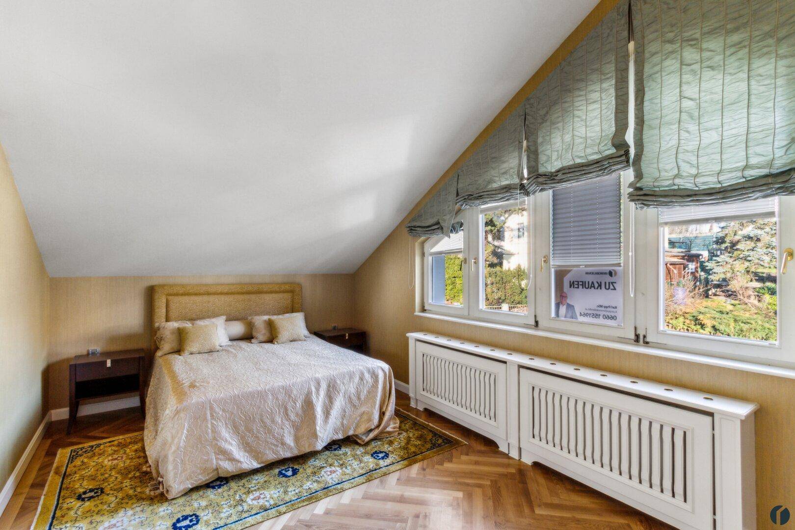 Gemütliches Schlafzimmer im Dachgeschoss mit schrägen Wänden, Parkettboden und Blick ins Grüne.