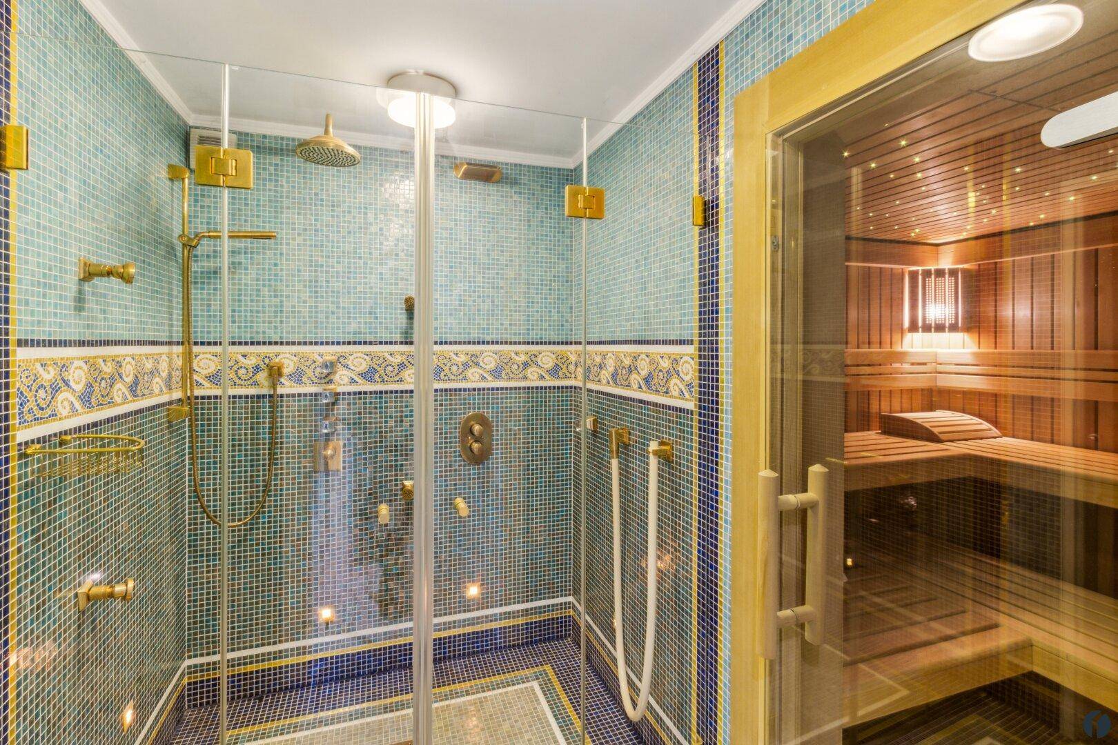Luxuriöser Wellnessbereich mit großer Dusche und angrenzender Sauna, ausgestattet mit goldenen Armaturen.