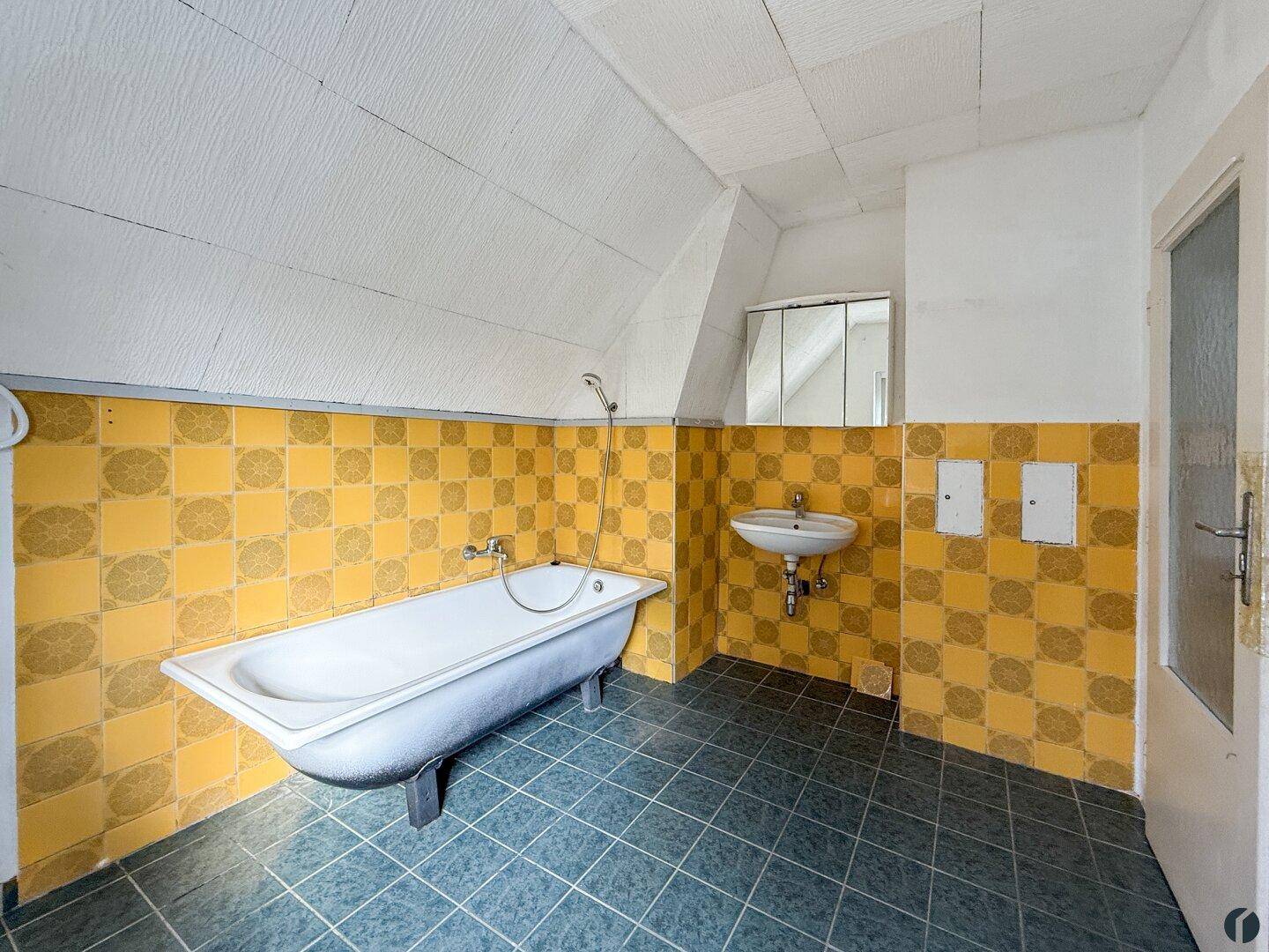 Badezimmer mit Badewanne, Waschbecken und gelb-gemusterten Fliesen im 80er-Jahre-Stil.