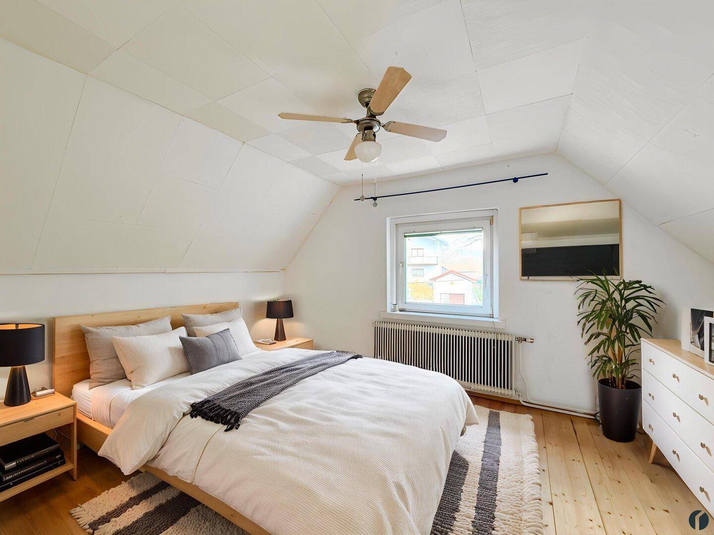 Gemütliches Schlafzimmer im Dachgeschoss mit Holzboden, Deckenventilator und schrägen Wänden.