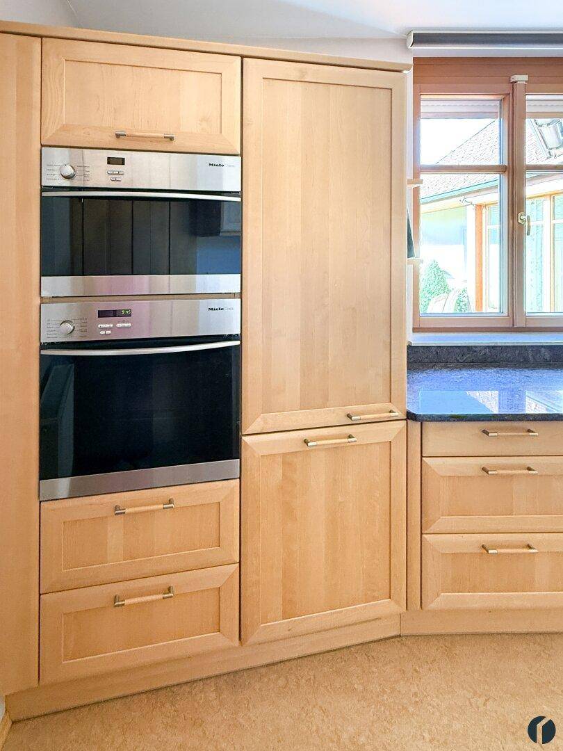 Hochwertige Einbauküche mit Miele Backofen und Mikrowelle in hellen Holzschränken.