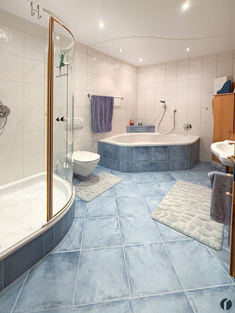 Modernes Badezimmer mit blauen und weißen Fliesen, Eckbadewanne und Duschkabine.