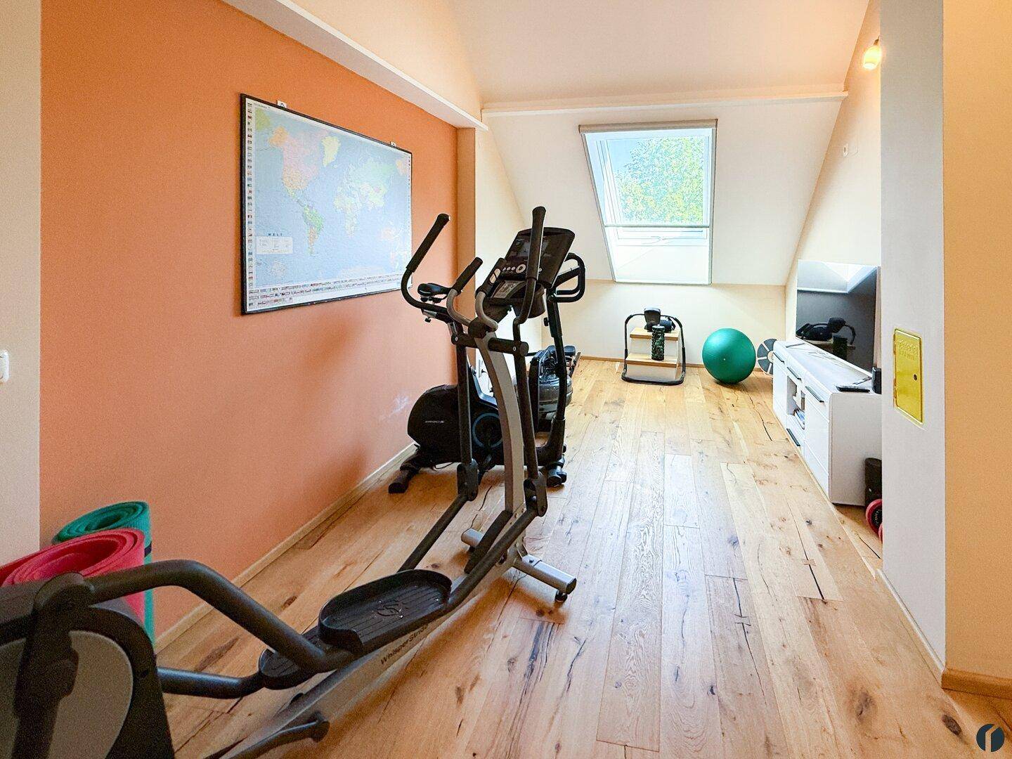 Geräumiger Fitnessbereich im Dachgeschoss mit verschiedenen Trainingsgeräten und Holzboden.
