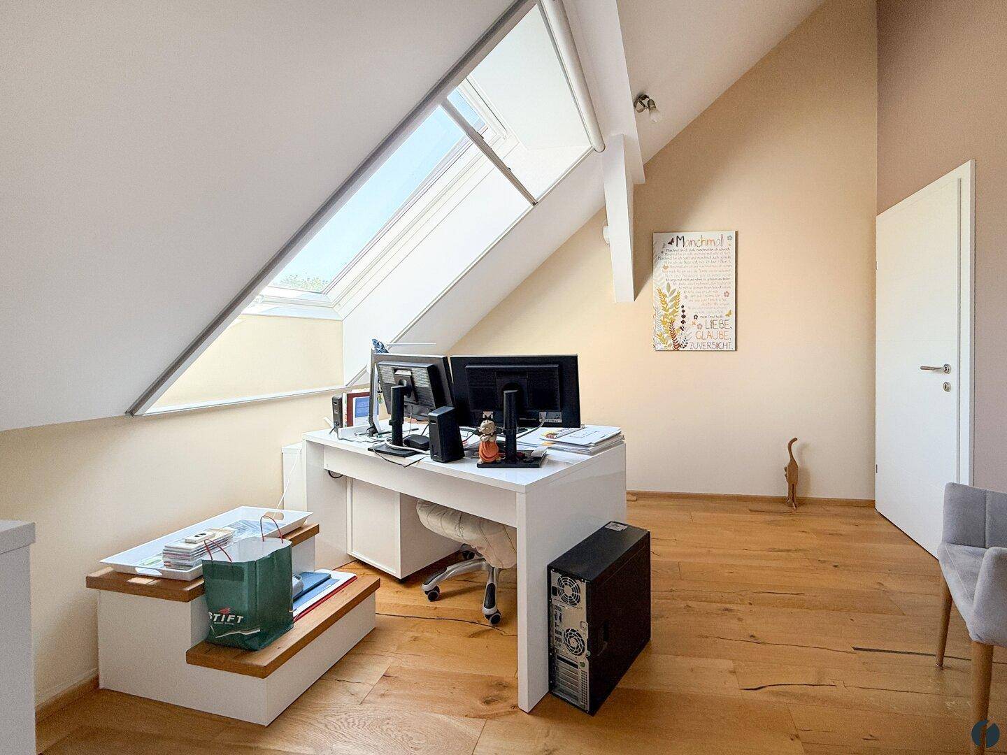 Geräumiges Arbeitszimmer im Dachgeschoss mit Schreibtisch, zwei Monitoren und Holzboden.