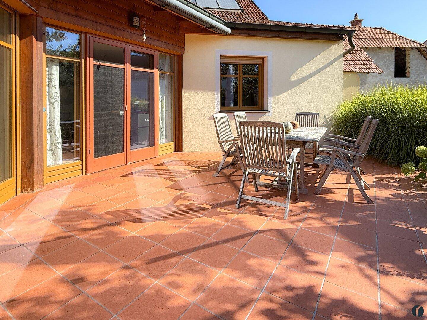 Große geflieste Terrasse mit Holztisch und Stühlen, ideal für Mahlzeiten im Freien.