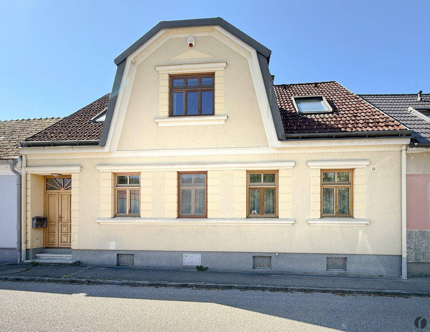 Historische Hausfassade mit Mansarddach und mehreren Fenstern zur Straße hin.