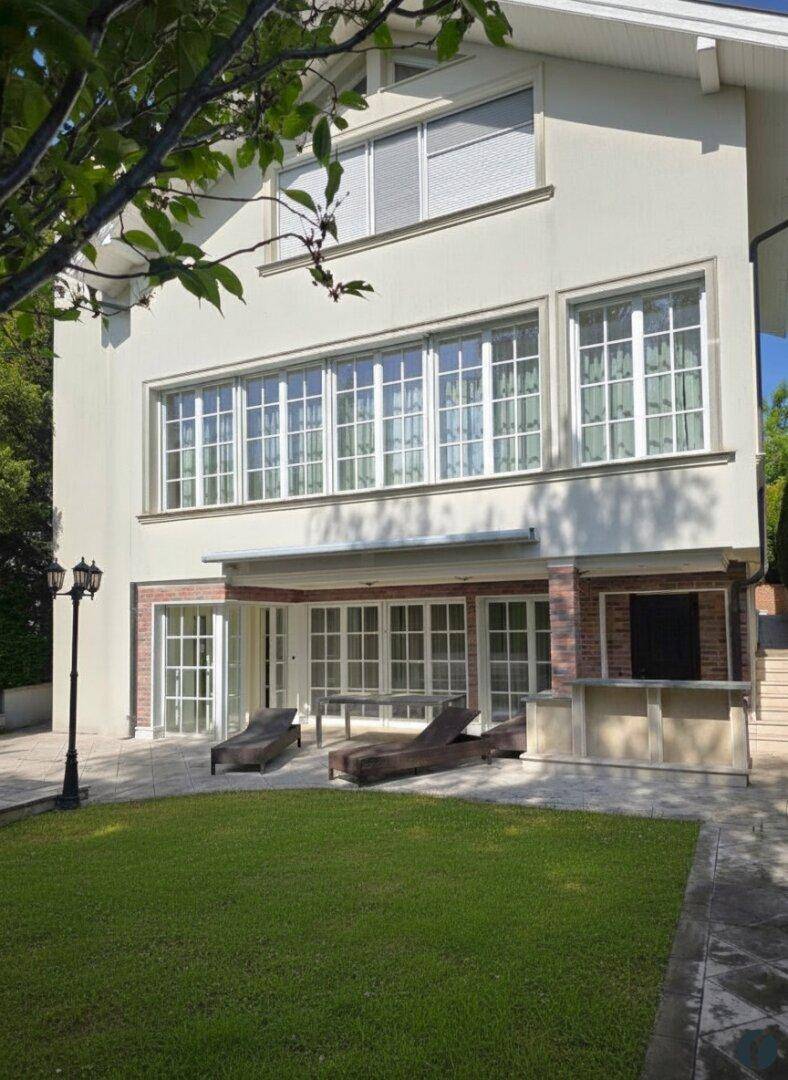 Moderne Hausfassade mit großen Fenstern und einer sonnigen Terrasse mit Liegestühlen.