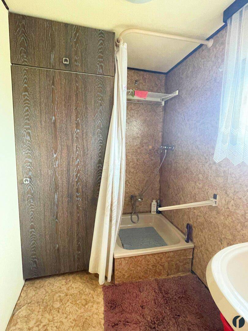 Badezimmer mit kleiner Badewanne, Duschvorhang, Waschbecken und einem Fenster.