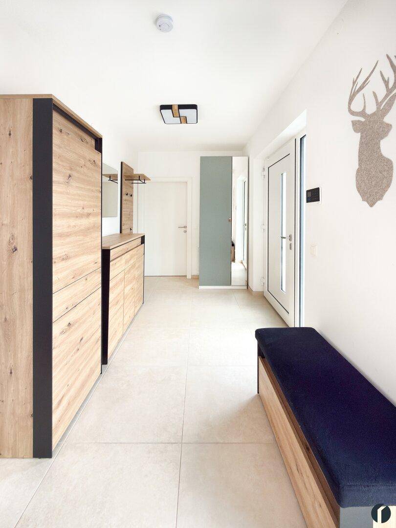 Heller Eingangsbereich mit Fliesenboden, Holzmöbeln und Hirsch-Wanddekoration.