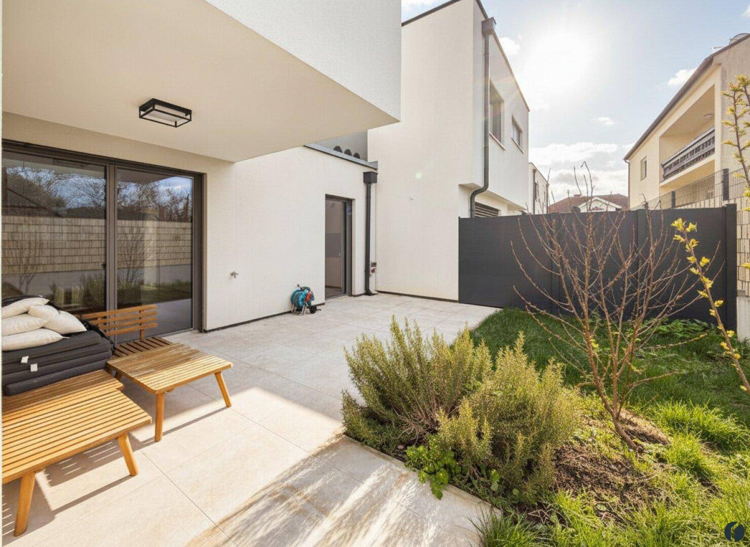 Sonniger Gartenbereich mit Terrasse, Rasenfläche und Sitzgelegenheiten am Haus.