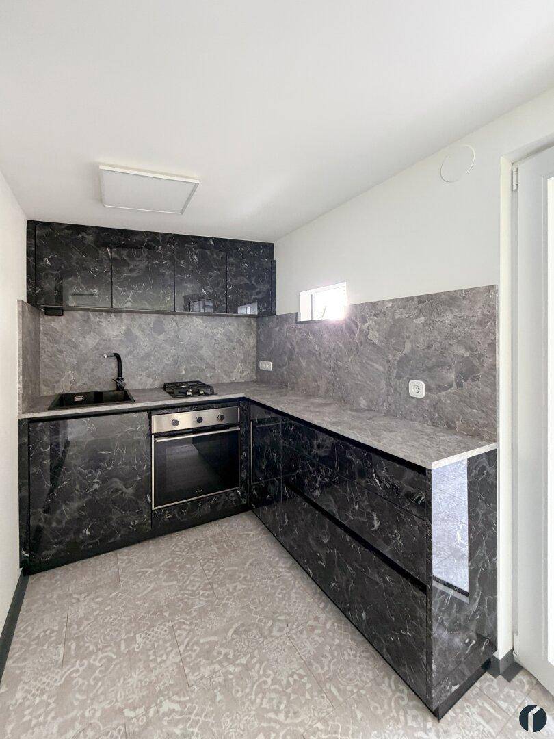 Moderne Küche mit dunklen Marmor-Effekt-Fronten, Gasherd und Fliesenboden.