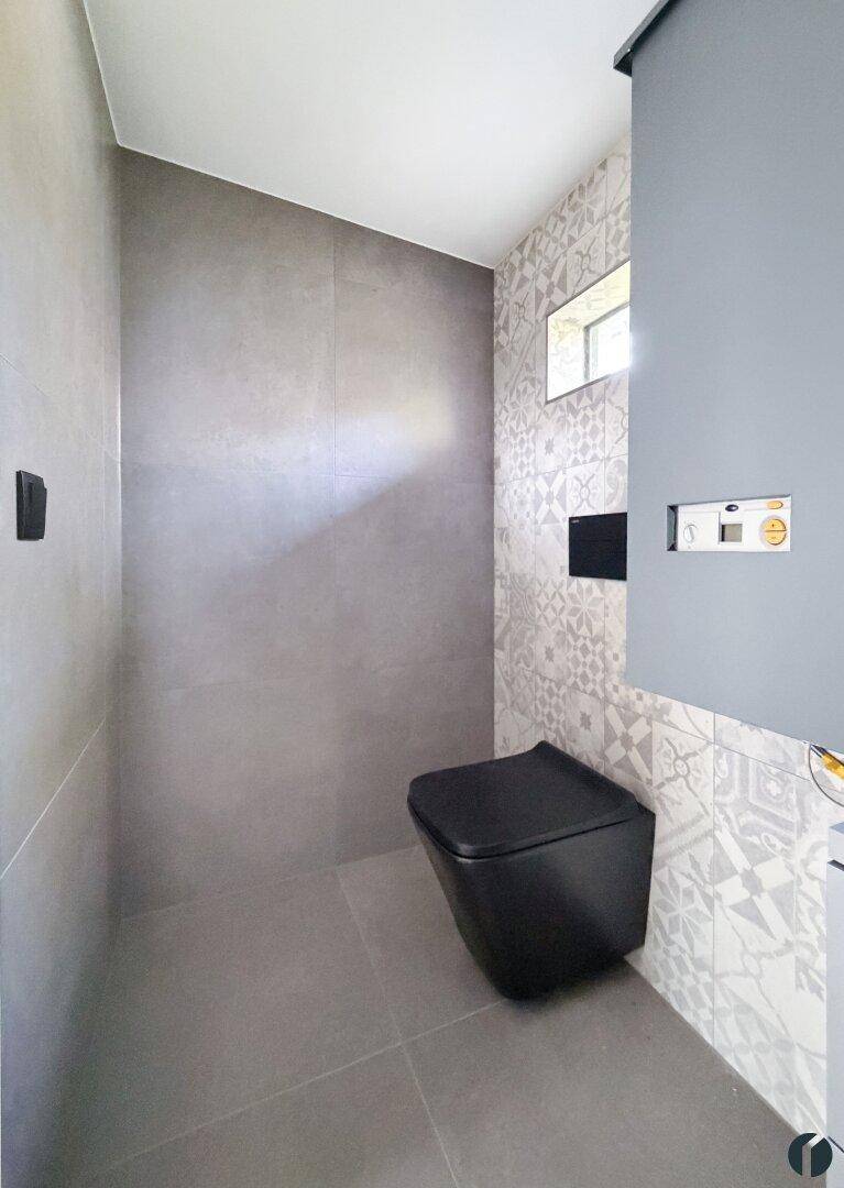 Separates WC mit moderner Wandtoilette und dekorativen Fliesen an der Wand.