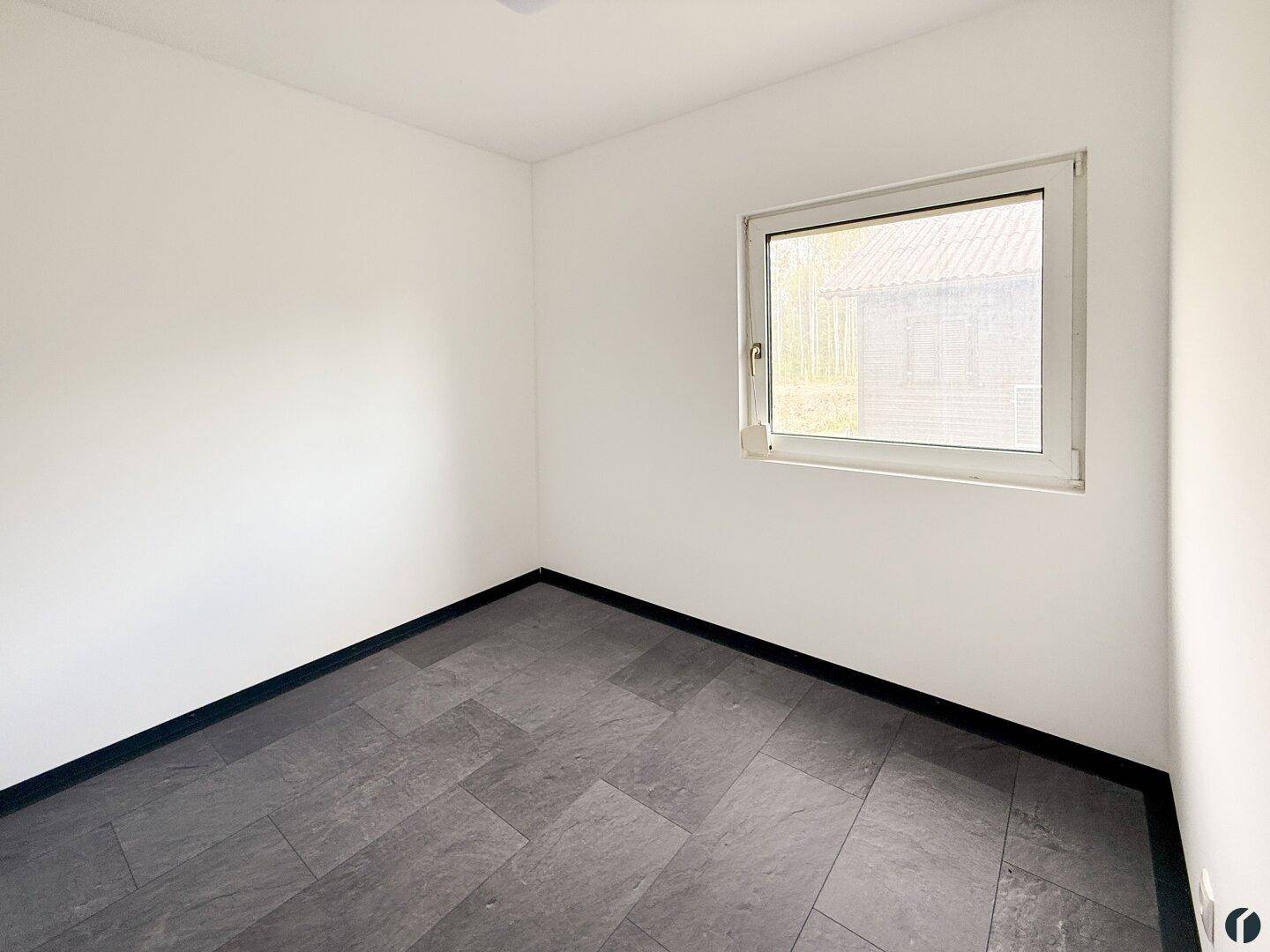 Helles Zimmer mit schlichten weißen Wänden und dunklem Fliesenboden.