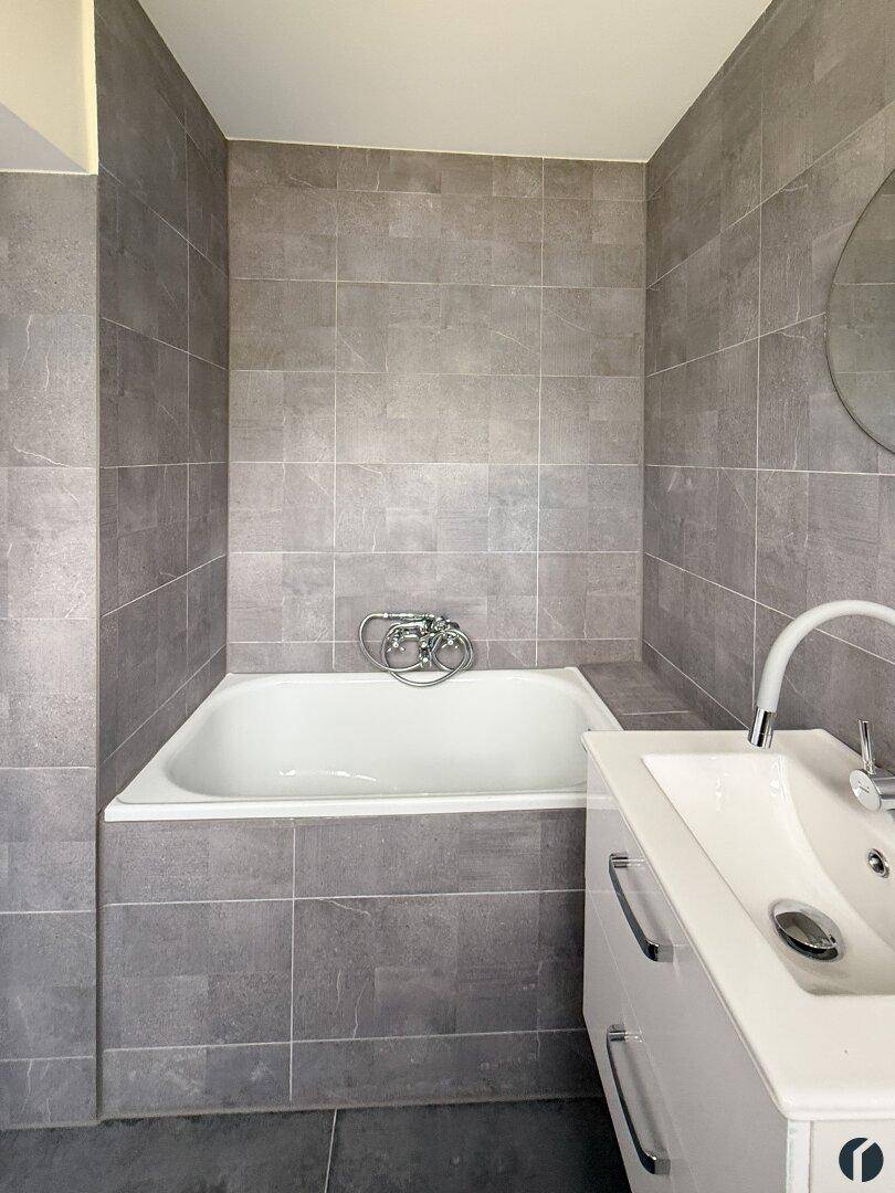 Badezimmer mit integrierter Badewanne, modernem Waschbecken und grauen Wandfliesen.