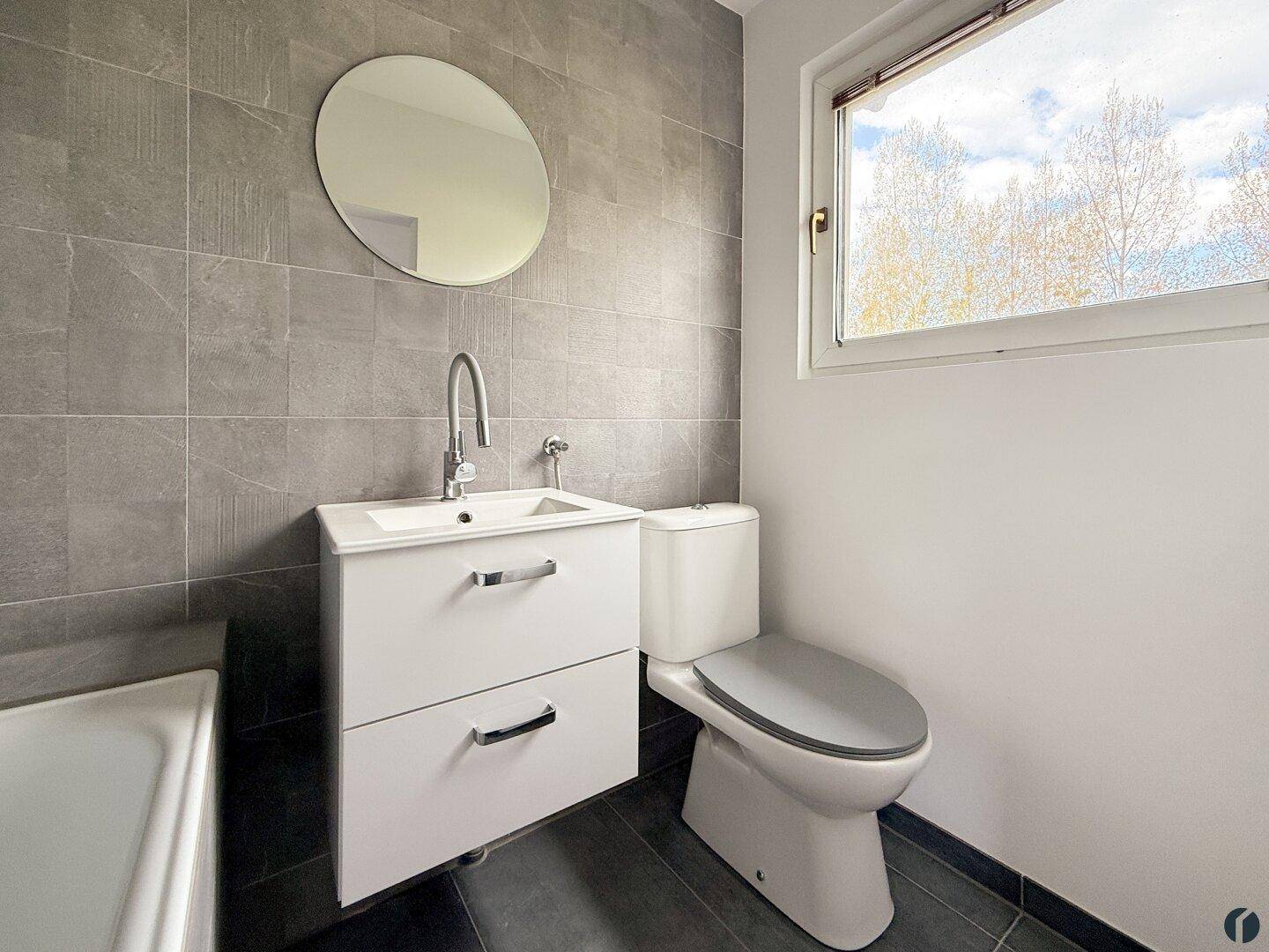 Modernes Badezimmer mit grauen Fliesen, Waschbecken, Toilette und Fenster.