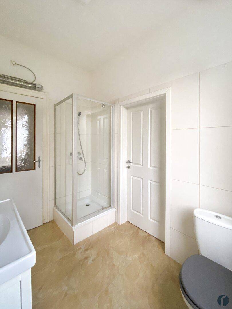 Badezimmer mit Duschkabine, WC und hellen Fliesen an Wänden und Boden.