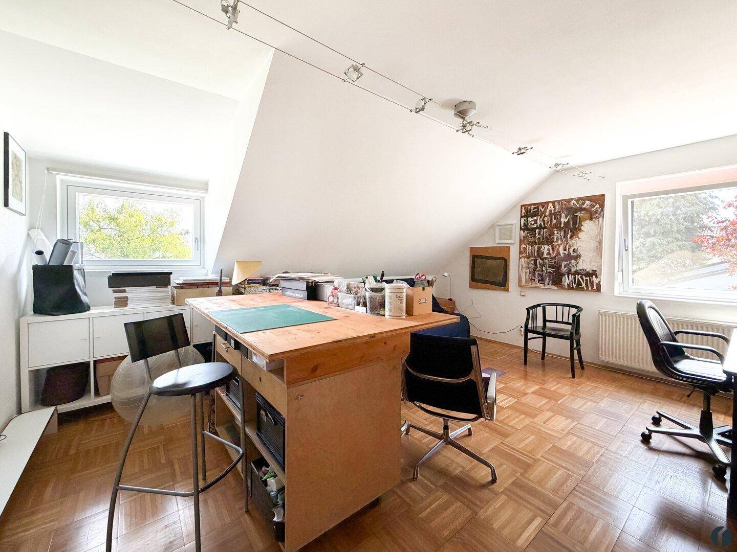 Kreatives Arbeitszimmer im Dachgeschoss mit großem Arbeitstisch und viel Tageslicht.
