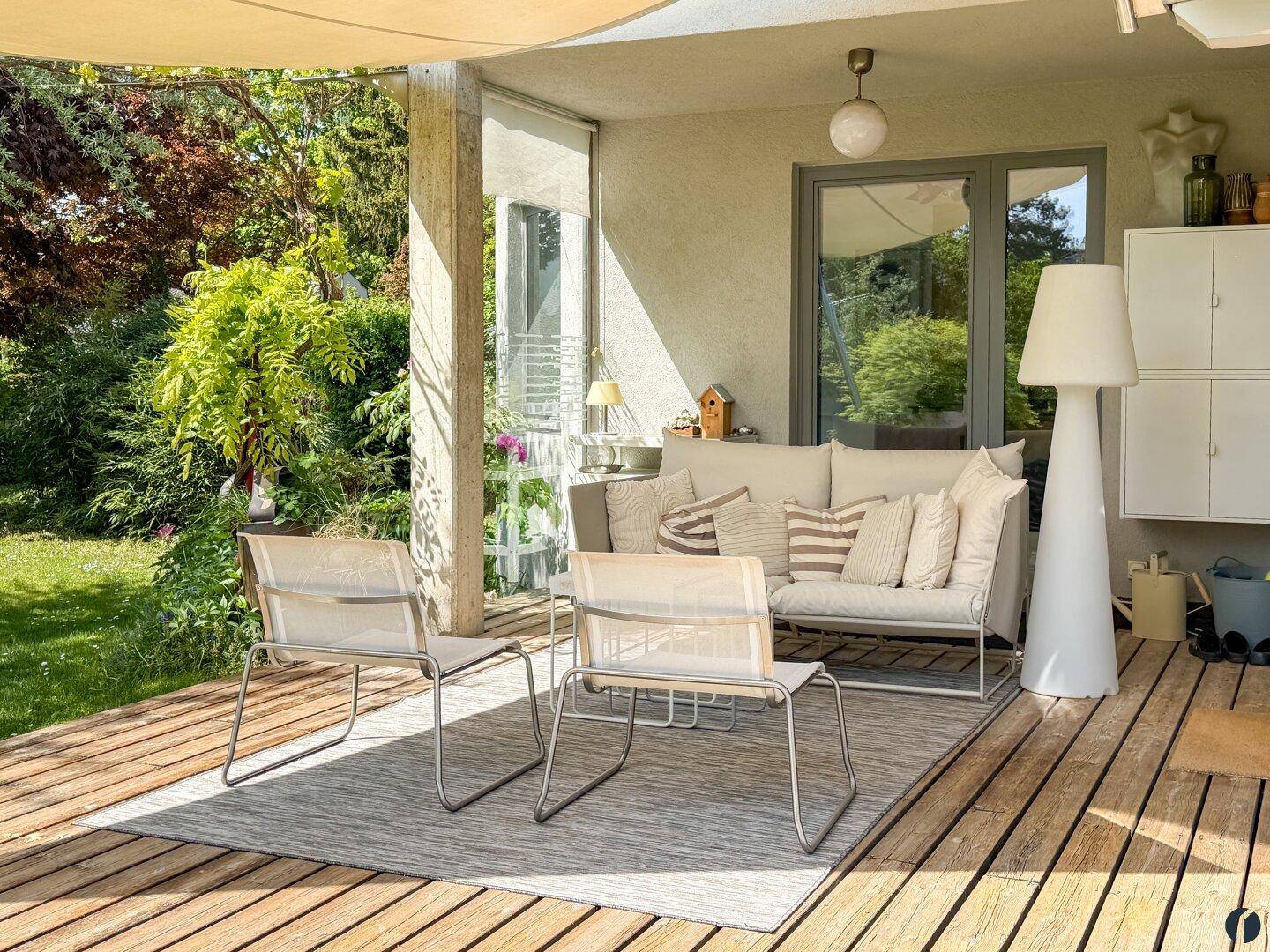 Entspannter Außenbereich auf einer Holzterrasse mit bequemen Gartenmöbeln und Sonnenschutz.