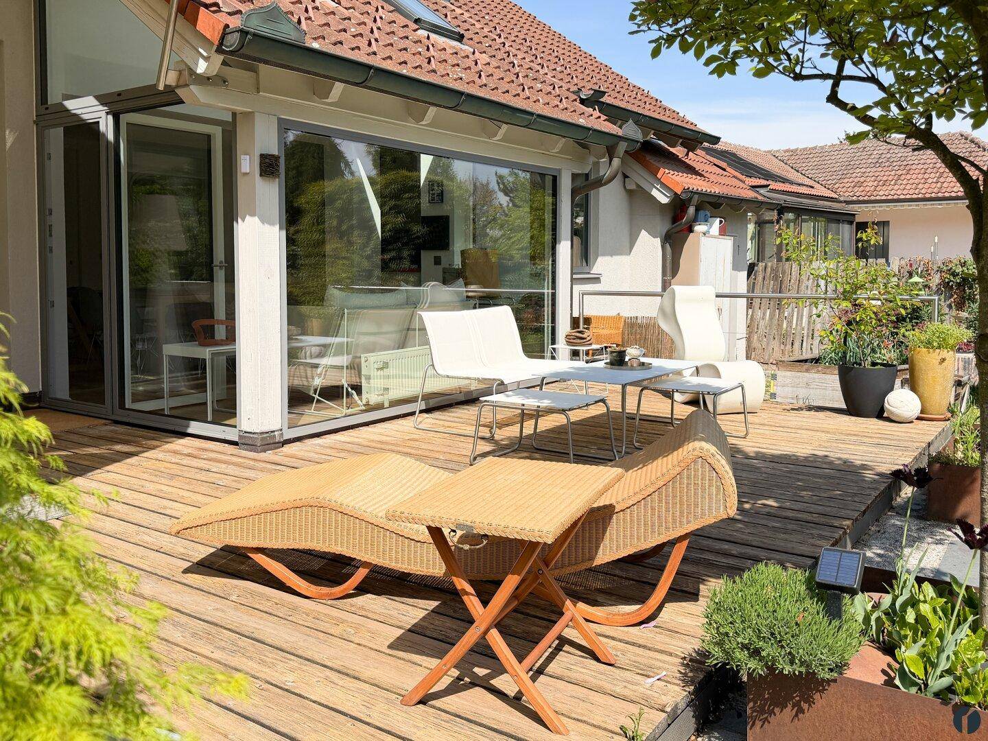 Großzügige Holzterrasse mit Sonnenliegen und Essbereich, umgeben von viel Grün.