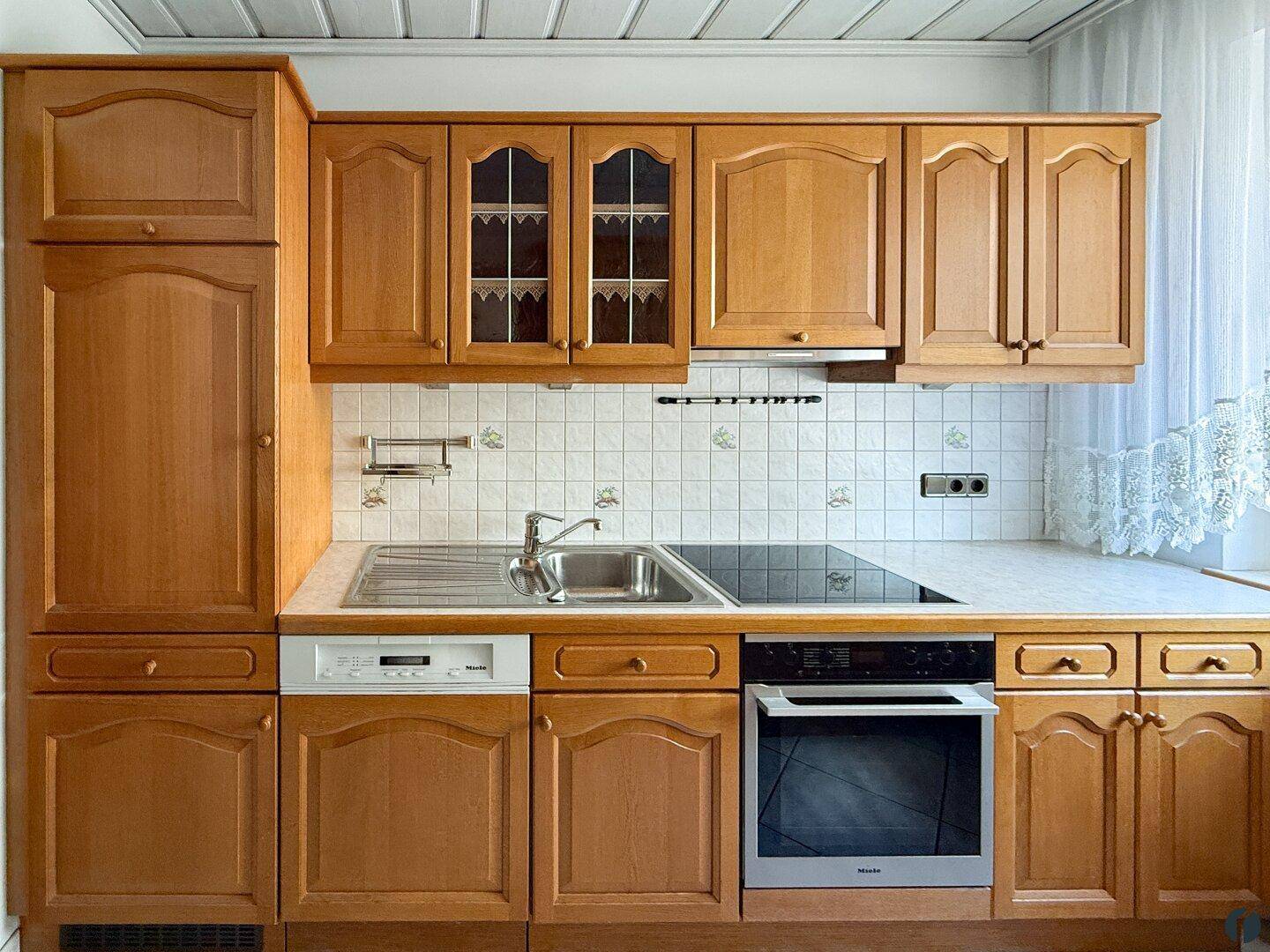 Traditionelle Holzküche mit Einbaugeräten wie Backofen, Geschirrspüler und Induktionskochfeld.
