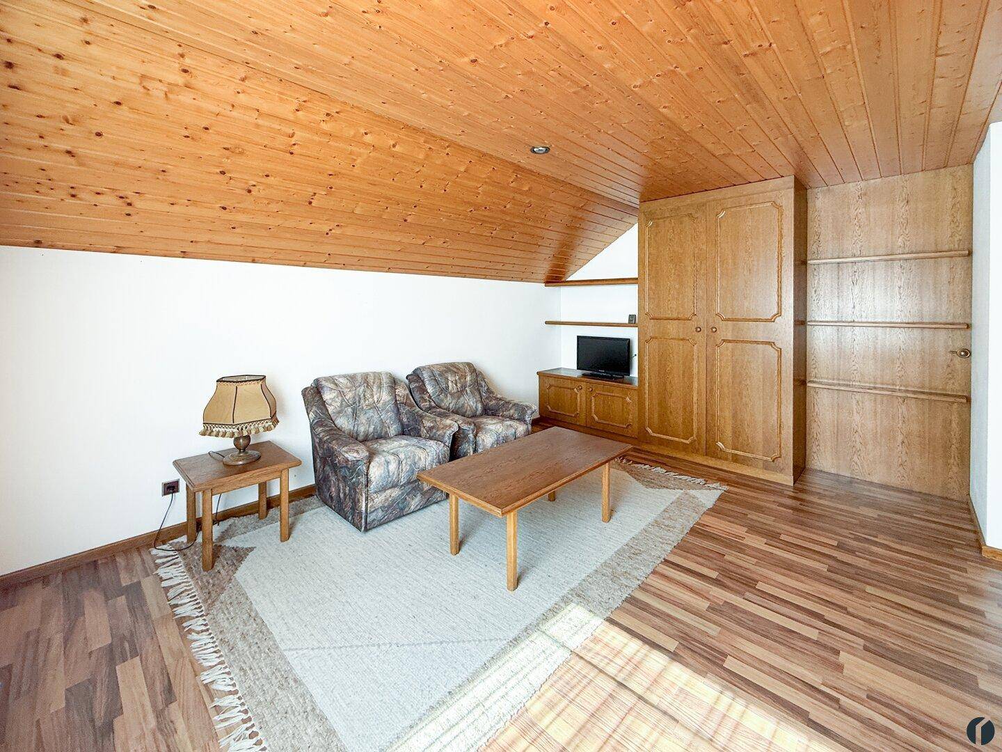 Gemütlicher Dachbodenraum mit Holzverkleidung an der Decke und Laminatboden.