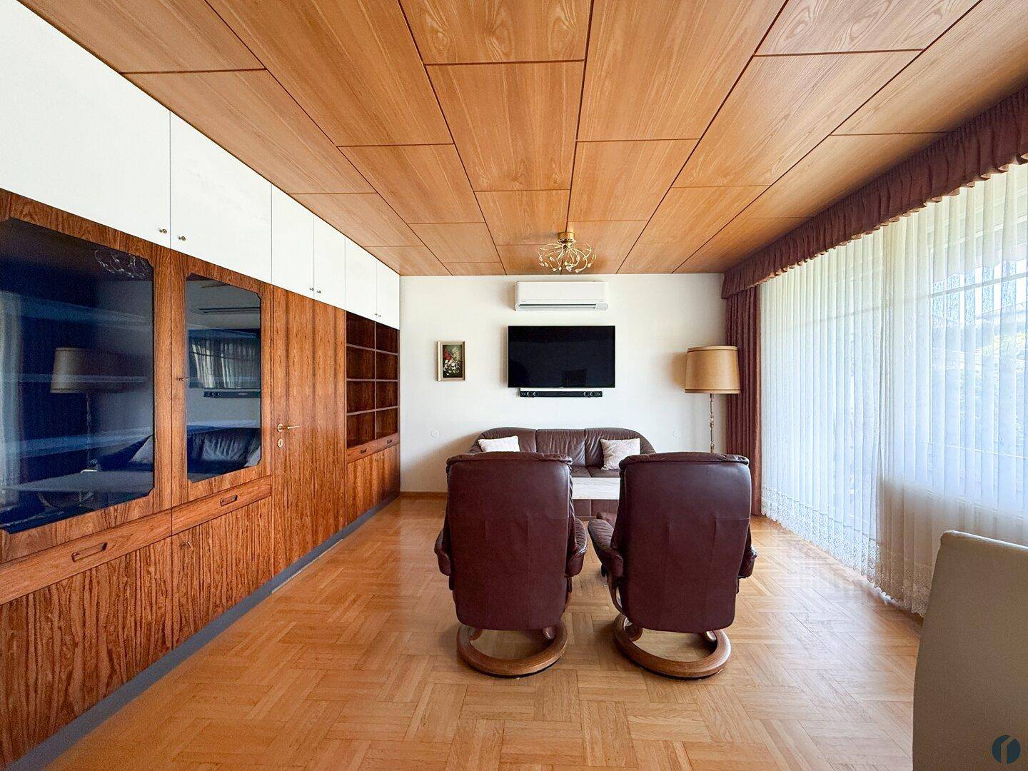 Wohnzimmer mit Holzdecke, Parkettboden, integrierten Schränken und Klimaanlage.