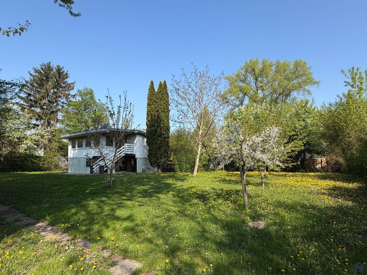 Freistehendes Haus umgeben von einem weitläufigen Garten mit blühenden Bäumen und Wiese.
