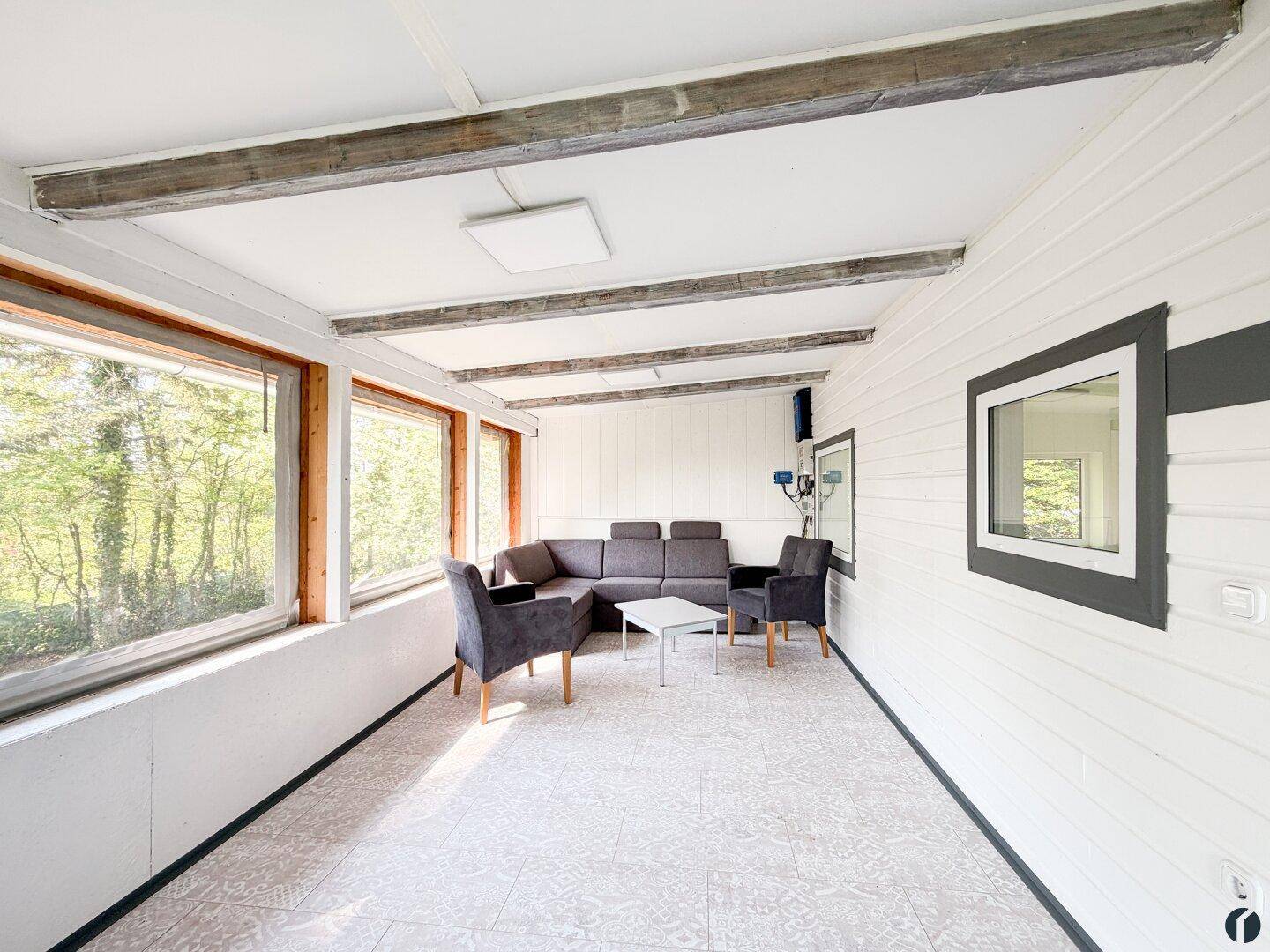 Helles Wohnzimmer mit großen Fenstern, Holzbalken und Blick ins Grüne.