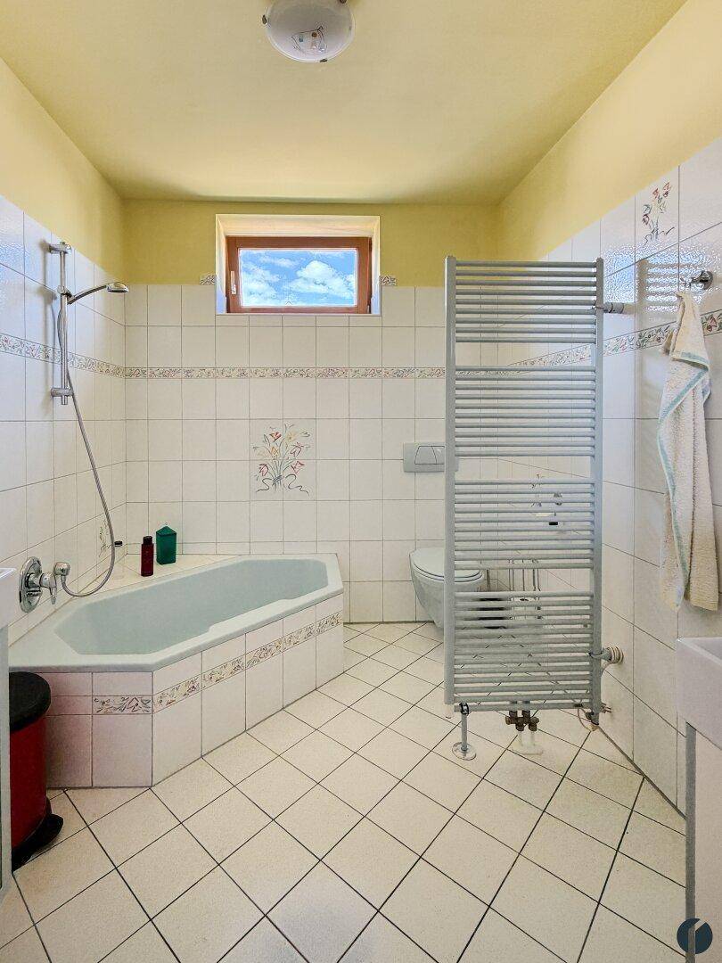 Badezimmer mit Eckbadewanne, Fliesenboden und beheiztem Handtuchhalter.