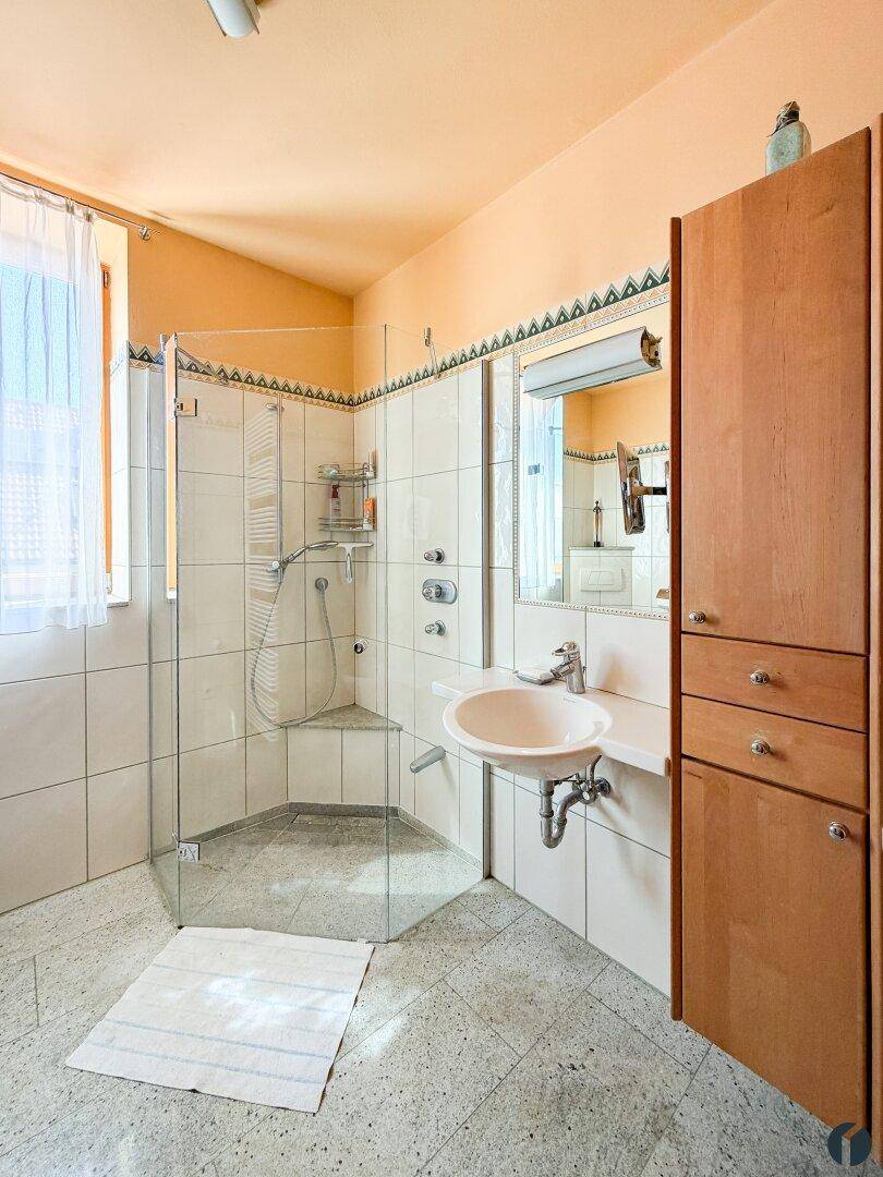 Modernisiertes Badezimmer mit begehbarer Dusche, Einzelwaschbecken und Holzschrank.