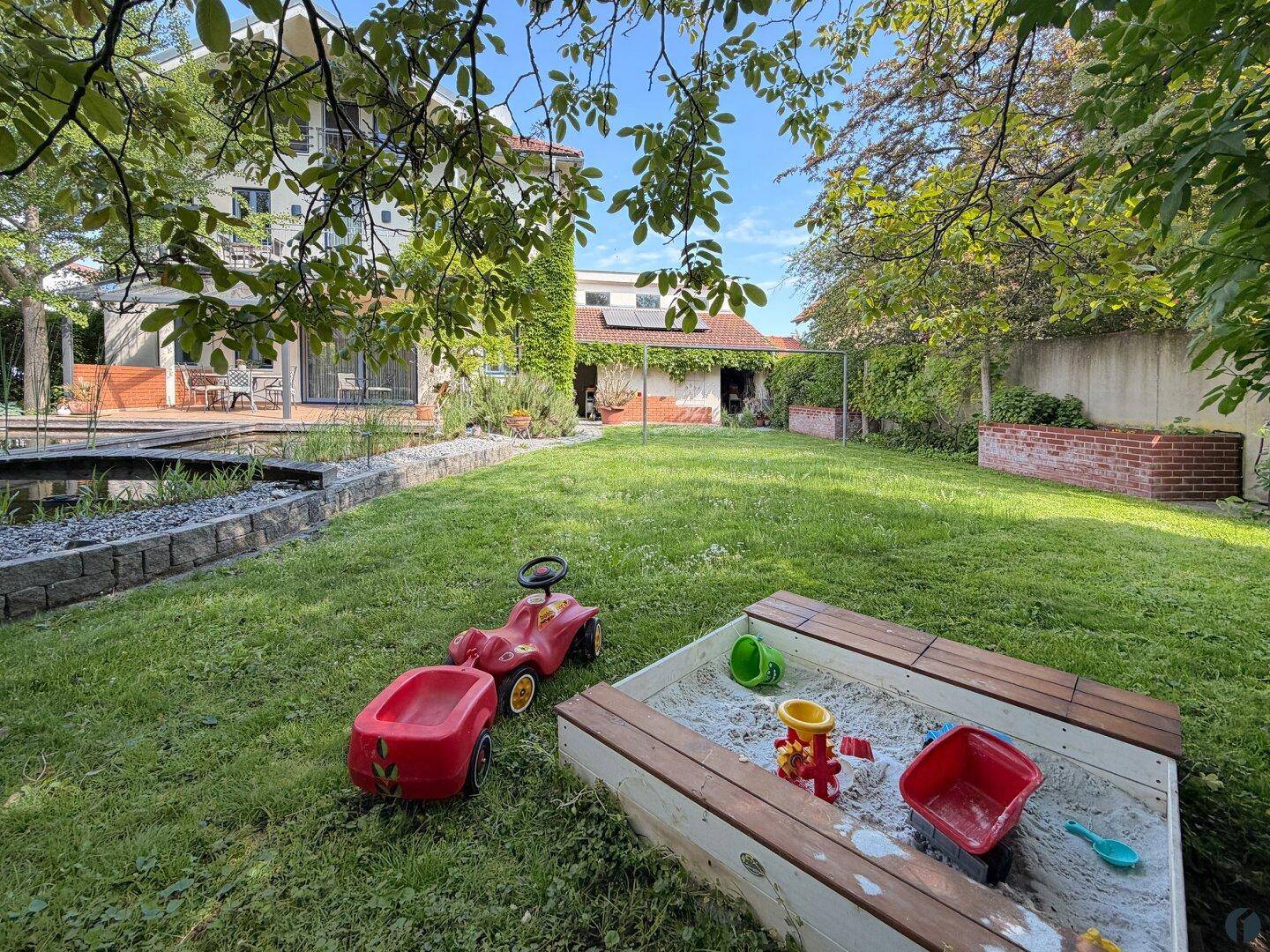 Großer Rasengarten mit Sandkasten und Spielzeug, ideal für Kinder.