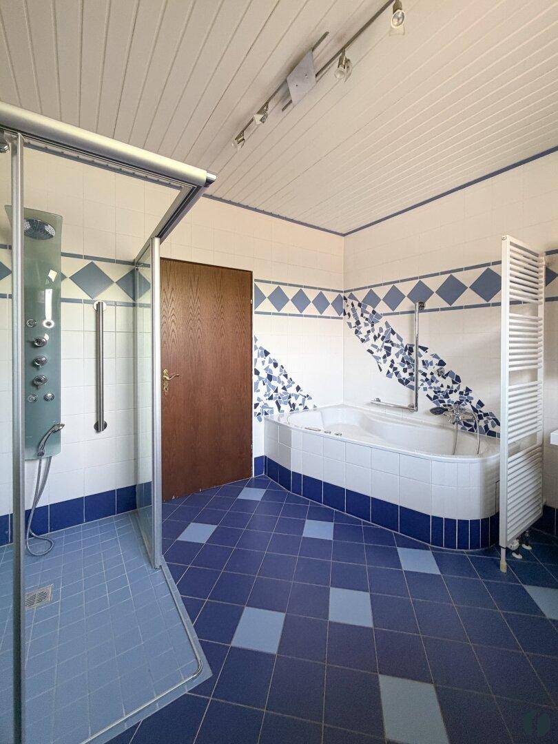 Badezimmer mit blauen Fliesen, Eckbadewanne und separater Duschkabine.