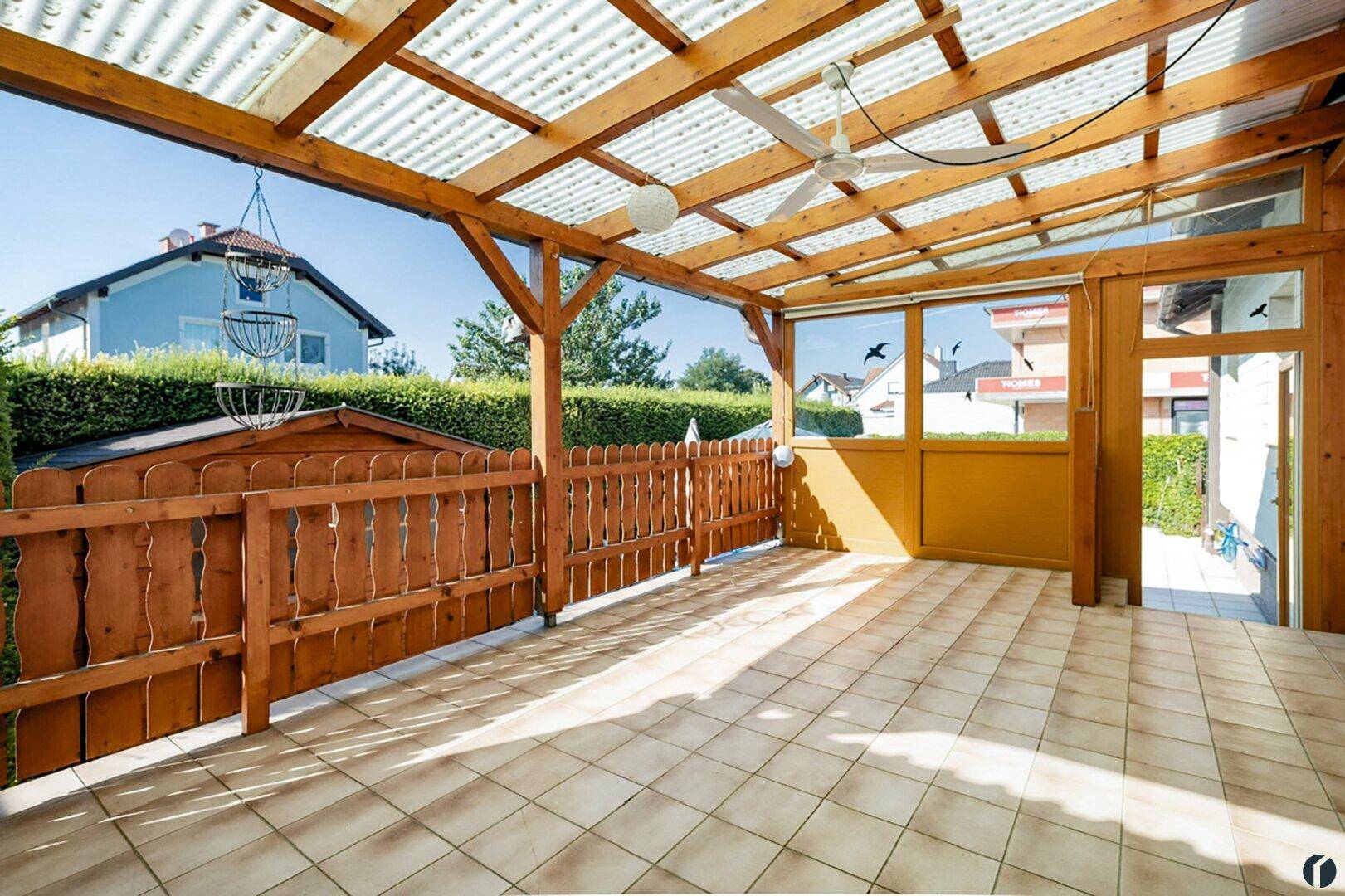 Überdachte Terrasse mit Holzkonstruktion, Fliesenboden und Deckenventilator.