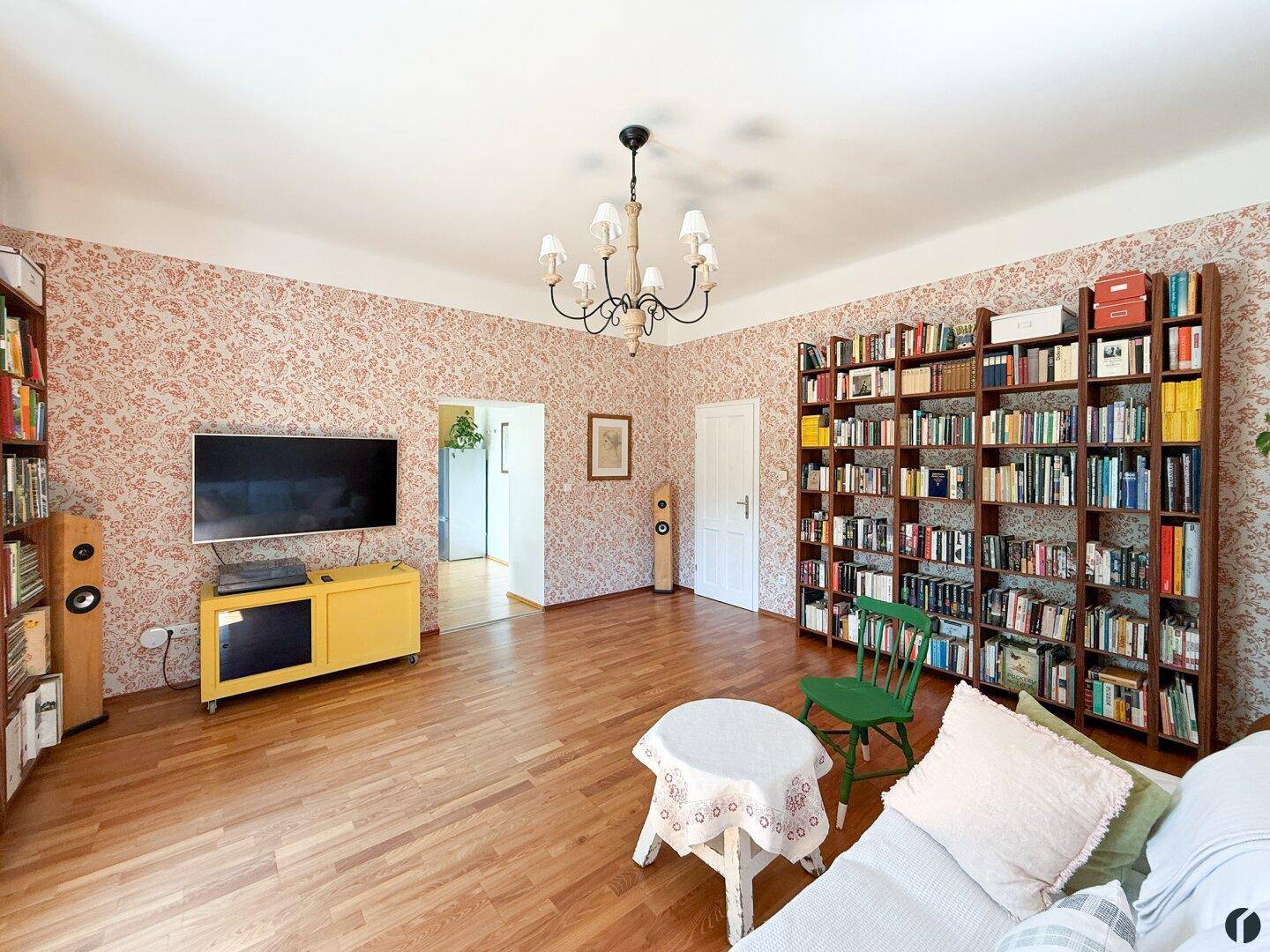Gemütliches Wohnzimmer mit gemusterter Tapete, Bücherregalen und Holzboden.